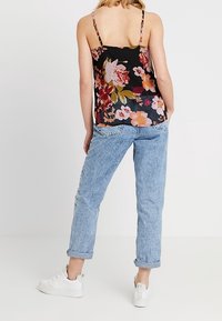 Camisole noire à motifs floraux avec bretelles spaghetti, associée à un jean boyfriend bleu clair retroussé et des baskets blanches. Tenue décontractée.