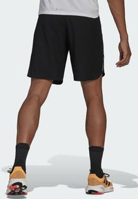 Shorts sportivi neri con un motivo testurizzato, abbinati a scarpe da corsa arancioni e nere, e calze nere a fantasia.