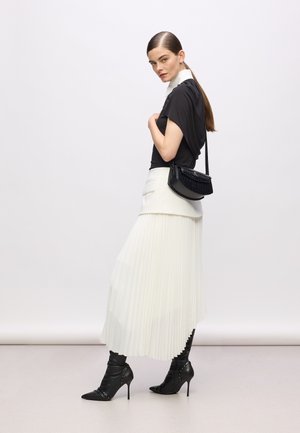 Black top with short sleeves, white pleated skirt, and black heeled boots with studded accents. Carrying a black crossbody bag.