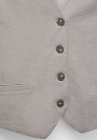 Chaleco de lino gris claro con seis botones oscuros, dos bolsillos laterales y solapa en pico, con una textura suave y forma entallada.
