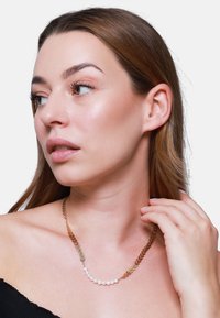 Collana d'oro con elementi a forma di foglia e perle disposte in una linea curva. Modella che indossa un top nero senza spalle.