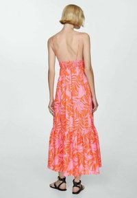 Robe maxi florale à dos nu, ornée de motifs de feuilles roses et oranges vives, avec une taille élastique et un ourlet à volants.