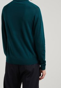 Pull tricoté couleur bleu sarcelle avec un col montant et des manches longues. Le dos présente une texture lisse et un ourlet côtelé, ajusté à la taille.