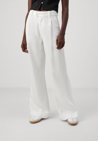 Zijden broek met een gestructureerde witte stof, voorzien van een aansluitende taille, riemlussen en een gladde afwerking, gecombineerd met witte schoenen.