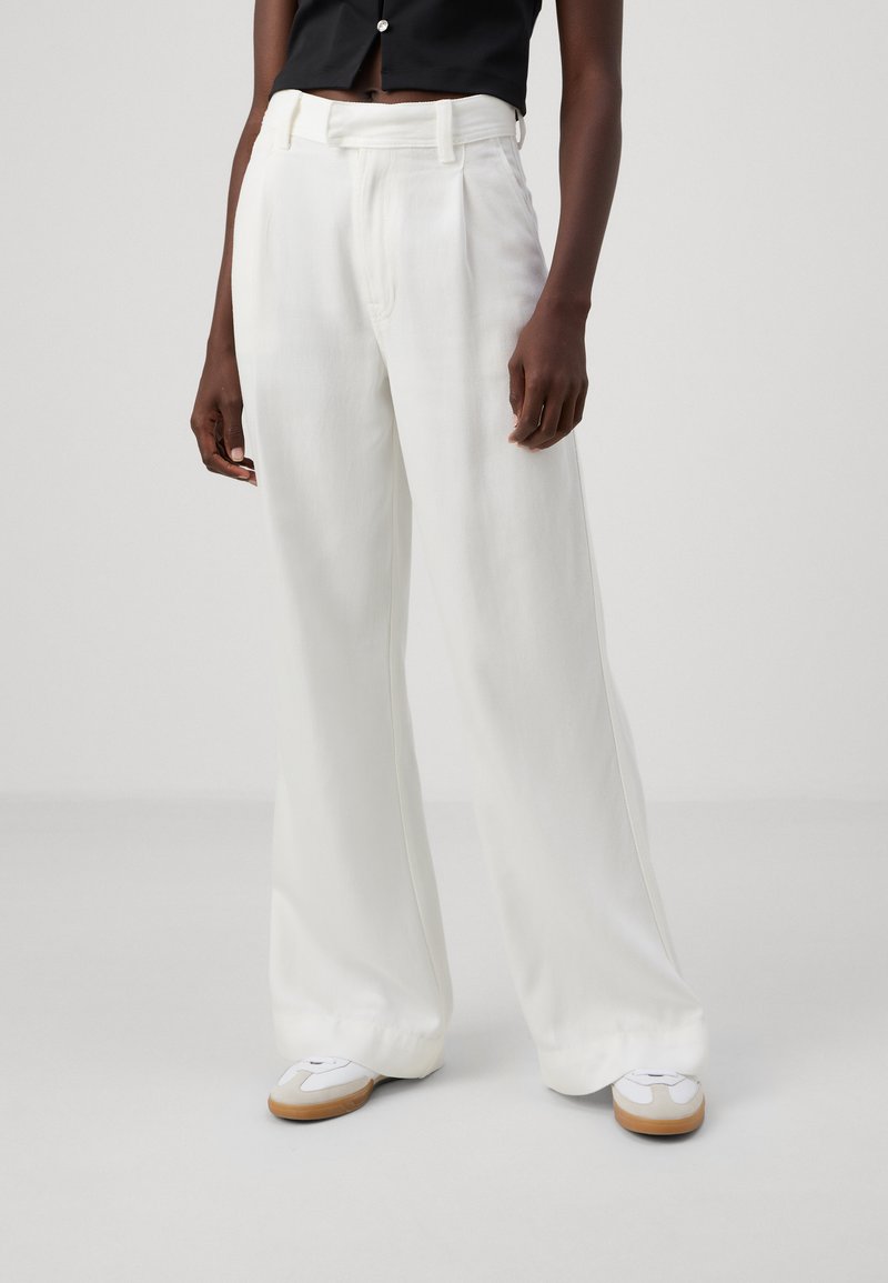 Zijden broek met een gestructureerde witte stof, voorzien van een aansluitende taille, riemlussen en een gladde afwerking, gecombineerd met witte schoenen.