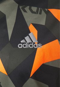 Camisa deportiva con un patrón geométrico en negro, gris y naranja. Logotipo de adidas en plata prominente en la parte inferior derecha. Tejido texturizado.