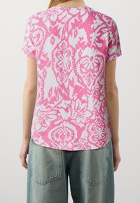 Top de manga corta con un patrón floral abstracto en rosa y blanco. Tejido ligero, dobladillo redondeado y un corte holgado.