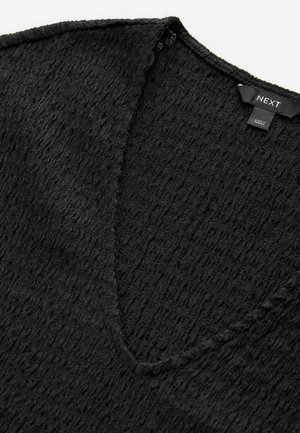 Sort tekstureret v-hals top med et subtilt krøllemønster, med en glat kant rundt om halsudskæringen og et mærke fastgjort bagpå.