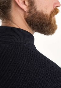 Marineblauer Strickpullover mit geripptem Kragen, der ein strukturiertes Muster und ein nahtloses Design an der Schulter aufweist, seitlich betrachtet.