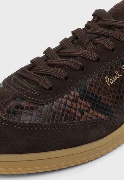 Gros plan d'une basket marron foncé en cuir texturé à motif serpent, lacets épais assortis, accents en daim et semelle en caoutchouc marron clair.