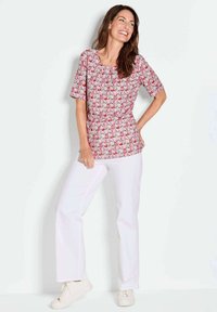 Korte mouwen roze top met een bloemenpatroon; gecombineerd met witte broeken en lichte schoenen. Soepele stof, comfortabele pasvorm, ronde hals.