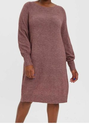 Mujer con un vestido de punto de manga larga color malva, con puños y dobladillo acanalados, de pie frente a un fondo claro y liso.