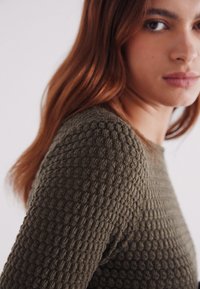 Olijfgroen, gemêleerd gebreid sweatshirt met een honingraatpatroon, voorzien van een ronde hals en aansluitende lange mouwen.