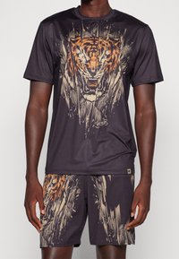 Man i svart sportset med stor rugande tigrer grafik i beige och orange på tröjan och shorts.