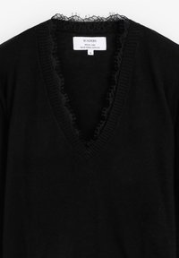 Suéter negro hecho de hilo suave, con un pronunciado escote en V adornado con encaje y detalles acanalados a lo largo del cuello. Etiqueta visible en el interior.