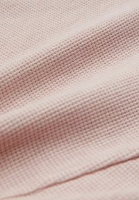 Țesătură cu textură de tip waffle, de culoare roz deschis, având un model în rețea și un finisaj moale, tactile, lăsându-se ușor pe suprafață.