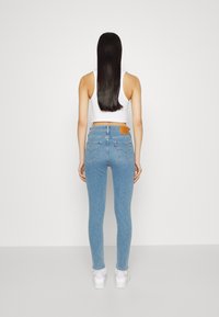 Vaqueros ajustados de color azul claro con cintura alta, cinco bolsillos y una etiqueta de cuero en la parte trasera. Combinados con un top corto blanco y zapatillas blancas.
