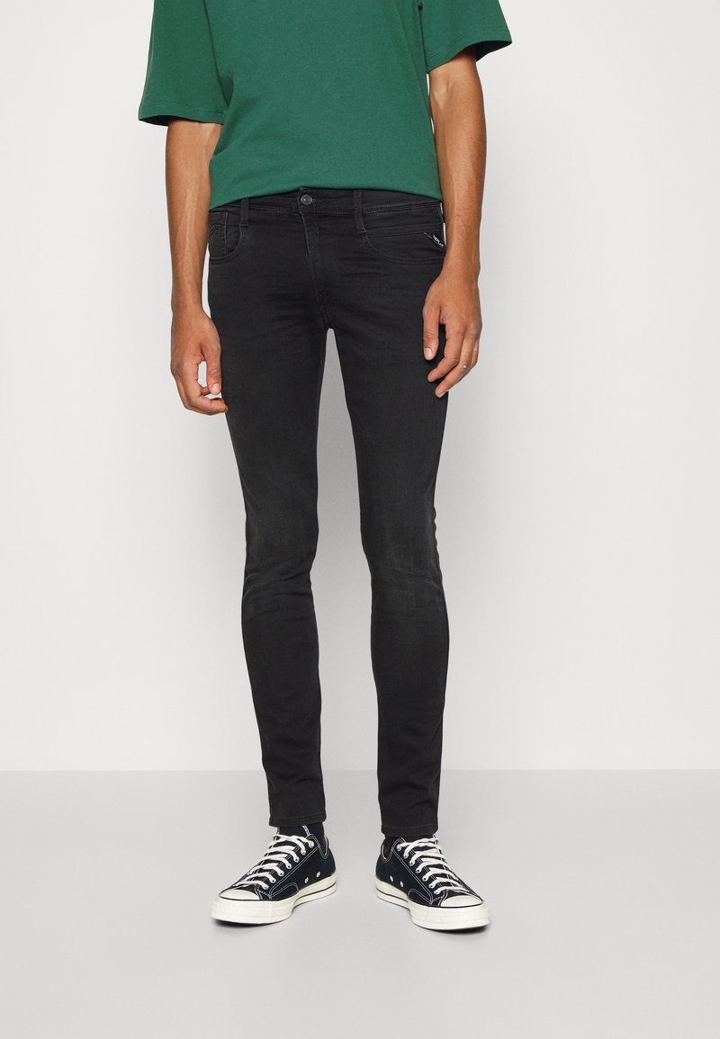 Jean skinny noir à texture lisse et design à cinq poches, assorti d'un t-shirt vert et de baskets noires à semelles blanches.