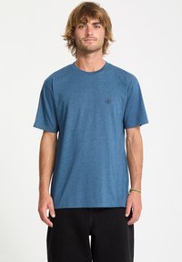 Blå kortærmet T-shirt lavet af blød stof, med rund hals og lille sort logo på venstre bryst. Casual pasform, minimalistisk design.