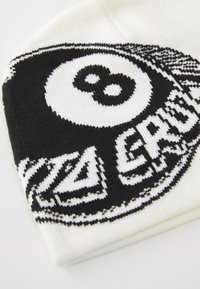 Gorro de punto en blanco y negro con un diseño de bola 8, que presenta un logotipo circular y acentos angulares, confeccionado en un suave material textil.