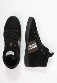 Baskets montantes en suède noir avec une bande d'accent vert, lacets plats, bout rond, étiquettes blanches de marque et semelles en caoutchouc.