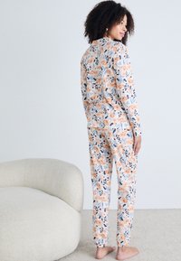 Blumiges Schlafanzug-Set in sanften Farben mit langen Ärmeln und elastischen Hosenbündchen. Mit orangefarbenen Blumen, grünen Blättern und einer weichen Stofftextur.