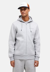 Gray zip-up hoodie in soft fabric with a kangaroo pocket, drawstrings, and ribbed cuffs. Paired with matching pants and a cap.
