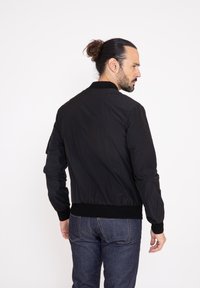 Svart bombarjacka i lätt material, med ribbad krage och muddar, dragkedjeförsedd framficka och elastisk midja.