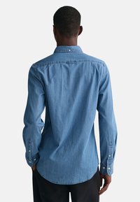 Lyseblå denimskjorte med lange ermer, standardkrage og knappemansjetter. Har en buet hem og en subtil tekstur.