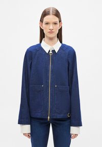 Μπλε σκούρο μπουφάν τζιν με φερμουάρ μπροστά, λευκό γιακά, δύο μπροστινές τσέπες και χρυσές λεπτομέρειες. Μανίκια raglan και λεία υφή.