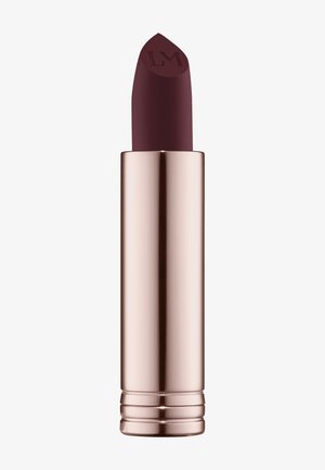 Rossetto borgogna opaco con una punta scolpita e un tubo metallico rosa oro. Presenta una consistenza liscia e un design con fondo arrotondato.