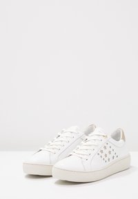 Vita läderskor med rund tå, med stjärnformade utskärningar på sidan, en beige häldetalj och en texturerad gummisul.