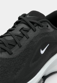 Crna atletska cipela s teksturiranim, mrežastim gornjim dijelom, vezicama i bijelim Nike logom. Ima bijeli međupodložak i crnu gumenu potplat.