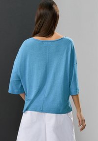 Maglietta in cotone blu a vestibilità ampia con scollo largo e maniche corte, caratterizzata da una texture morbida e un orlo dritto sul retro.