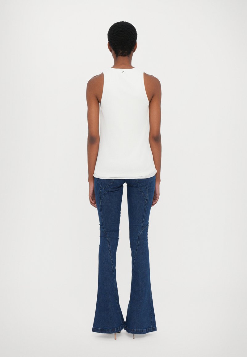 Top sin mangas blanco combinado con jeans acampanados azules. El top presenta un diseño sencillo; los jeans tienen costuras decorativas y un dobladillo acampanado.