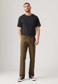 Black cotton t-shirt paired with olive green pants. The pants feature classic pockets, a zipper fly, and a straight-leg design. Black sneakers complete the look.