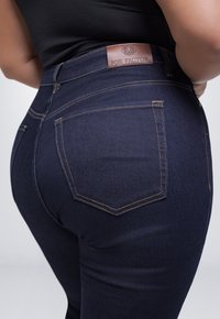 Donkerblauwe denim jeans met een strakke pasvorm, voorzien van een bruin leren label op de tailleband en gedetailleerde stiksels op de zakken.