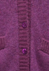 Πλεκτή ζακέτα σε πλούσιο μοβ χρώμα, με χοντρή υφή, ριμπ λεπτομέρειες και μεγάλα κουμπιά στο ίδιο χρώμα. Διαθέτει επίσης τσέπες.