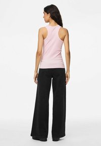 Top de tirantes de canalé rosa claro con un diseño de espalda nadadora, combinado con pantalones anchos negros y zapatos de plataforma negros.