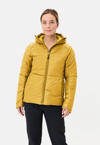 Giacca gialla isolata con cappuccio, dotata di tasche laterali con zip e design trapuntato. Texture liscia e forma aderente. Indossata con pantaloni neri.