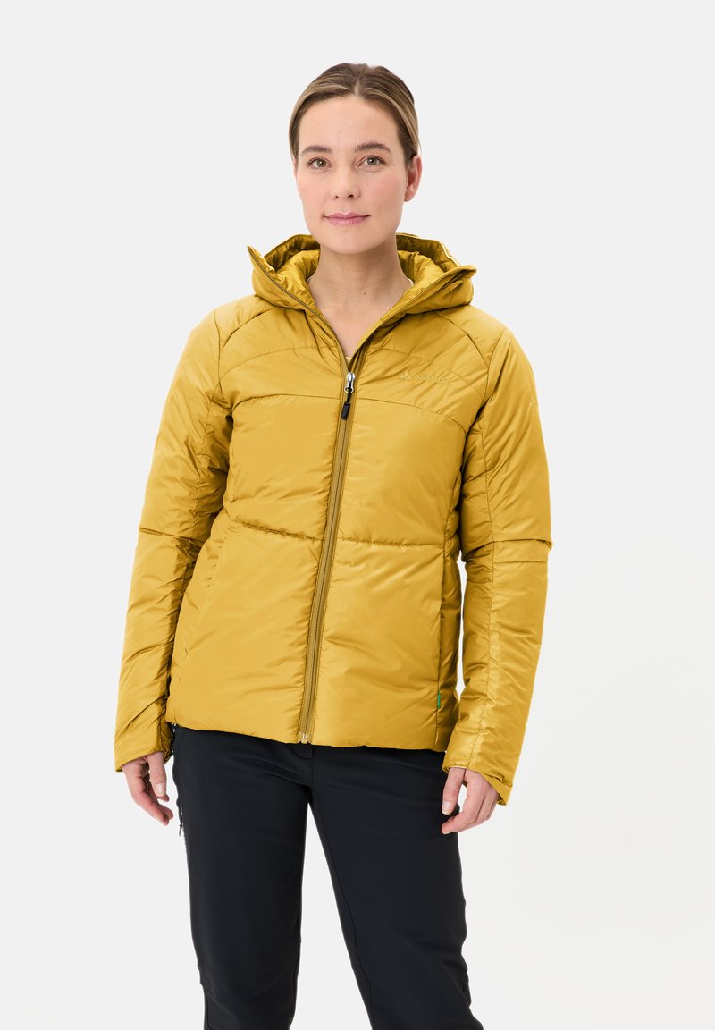 Giacca gialla isolata con cappuccio, dotata di tasche laterali con zip e design trapuntato. Texture liscia e forma aderente. Indossata con pantaloni neri.