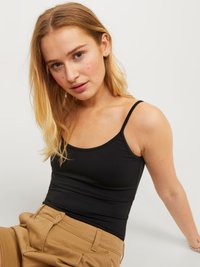 Top negru, fără mâneci, cu un design ajustat și o textură netedă. Este purtat cu pantaloni din bumbac bej, cu talie înaltă, având butoane vizibile.