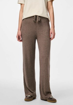 Personne porte un pantalon en maille marron ample et côtelé avec une taille à cordon et des chaussures marron foncé à enfiler, assorti à un haut beige à manches courtes.