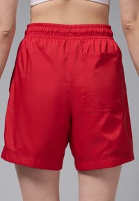 Rote Shorts aus glattem Stoff mit einem elastischen Bund und einer quadratischen Tasche auf der rechten Seite. Der Saum ist am unteren Rand umgeschlagen.