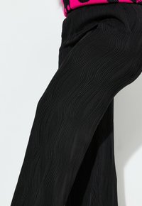 Pantaloni neri con un design a trama ondulata. Realizzati in un tessuto morbido, hanno una vestibilità rilassata con tasche sottili sui lati.