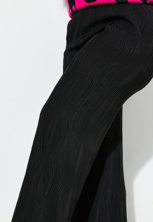 Schwarze Hose mit einem gewellten, strukturierten Design. Hergestellt aus einem weichen Stoff, haben sie einen lässigen Schnitt mit dezenten Taschen an den Seiten.