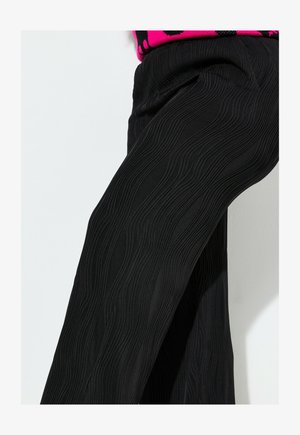 Schwarze Hose mit einem gewellten, strukturierten Design. Hergestellt aus einem weichen Stoff, haben sie einen lässigen Schnitt mit dezenten Taschen an den Seiten.