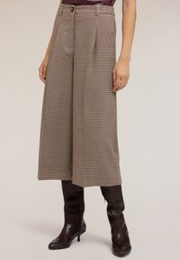 Pantalons larges en houndstooth marron avec taille haute, présentant une fermeture à bouton et des plis. Associés à des bottes marron montantes.