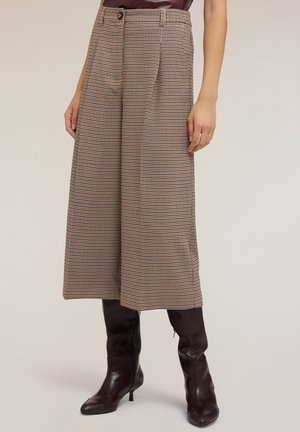 Pantaloni a palazzo in tessuto houndstooth marrone con vita alta, dotati di chiusura a bottone e pieghe. Abbinati a stivali marroni alti fino al ginocchio.