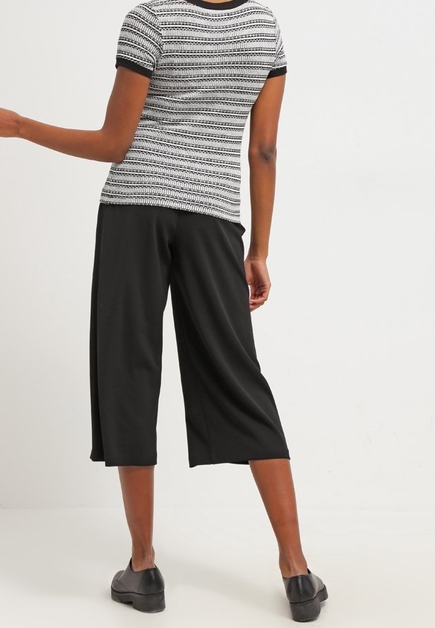 Černé kalhoty culottes s širokými nohavicemi, doplněné texturovaným topem s krátkým rukávem, který má černobílý vzor a kontrastní manžety.
